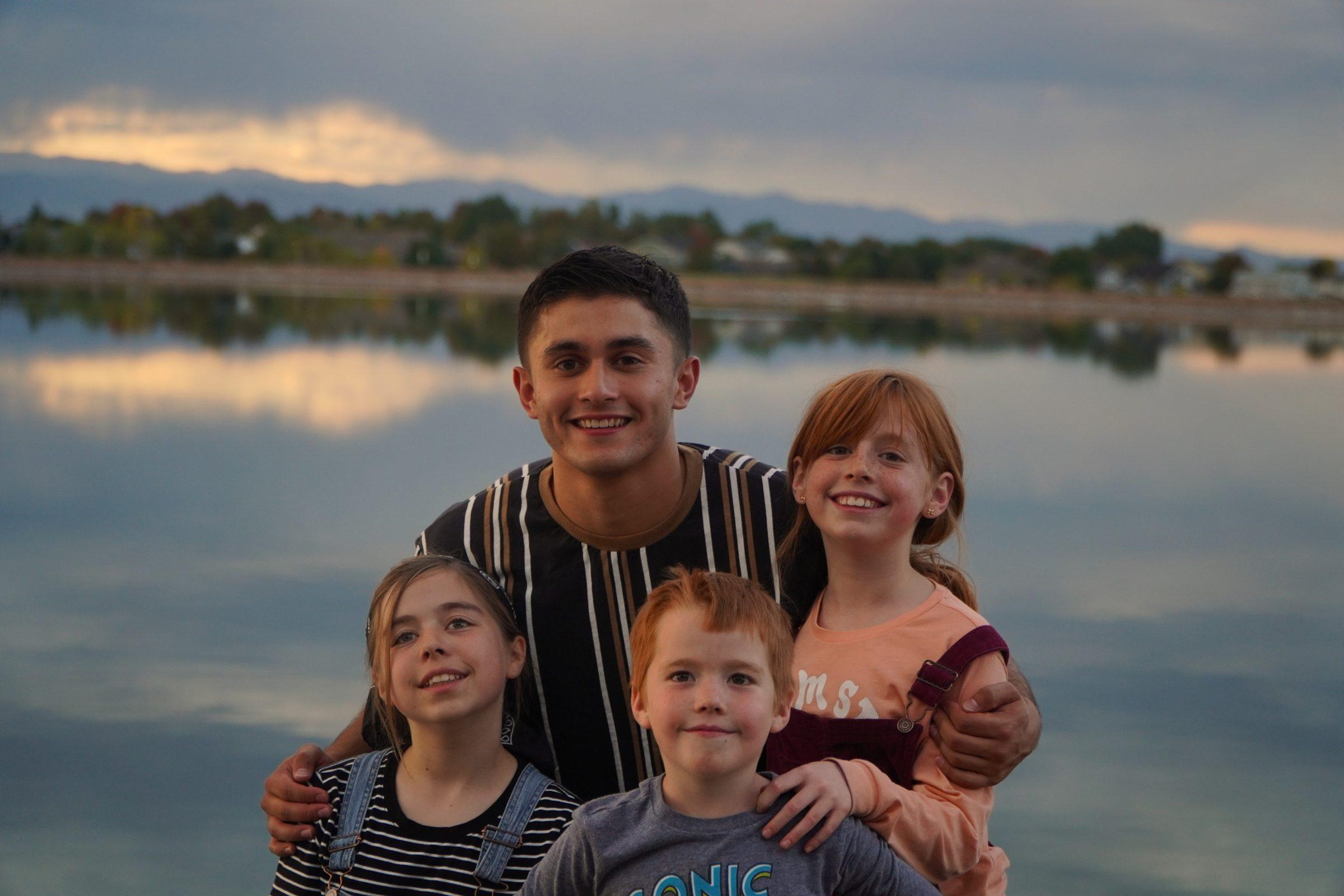 Young man with his three younger siblings by a lake at sunset