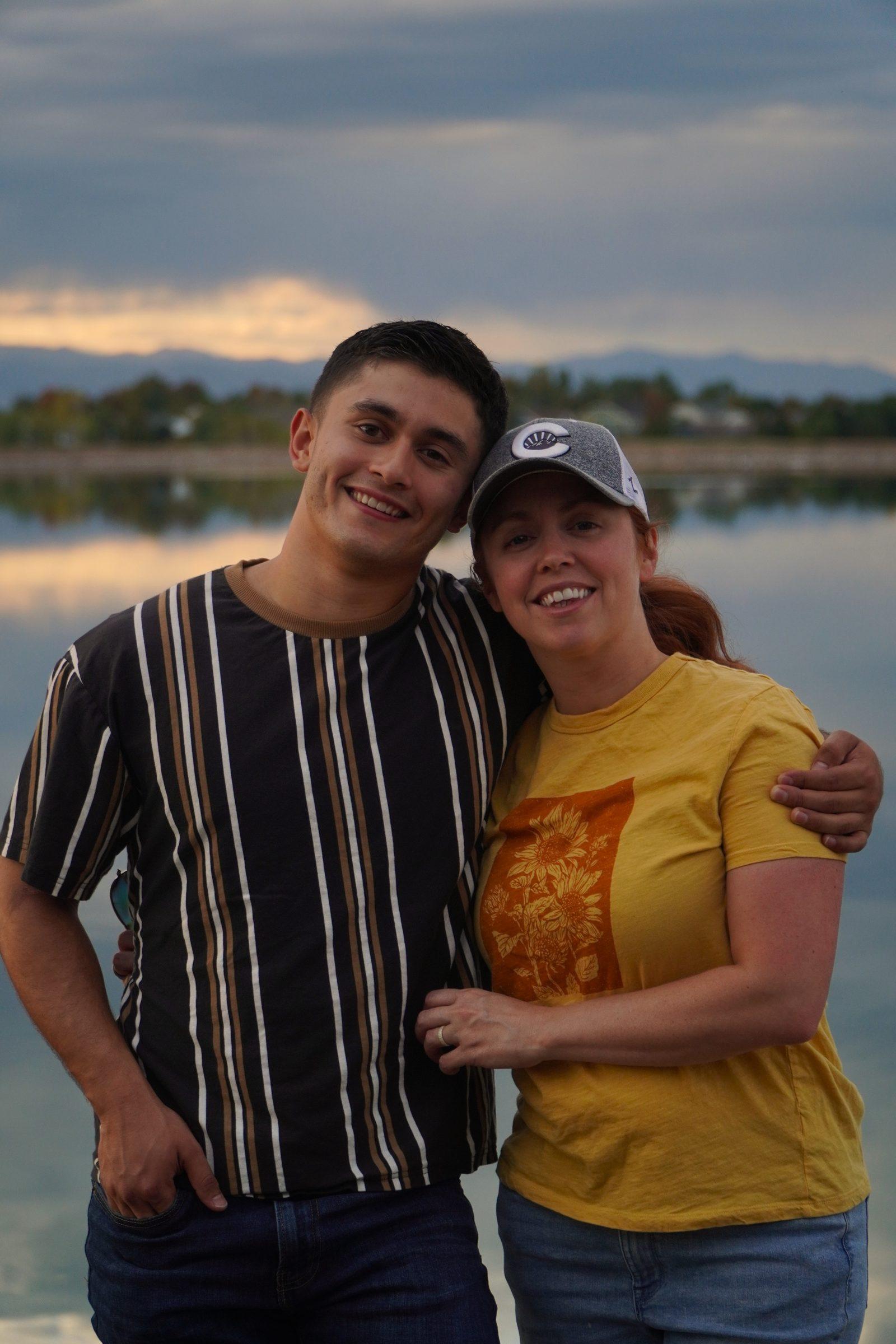 Young man and his mother posing together by a lake at sunset