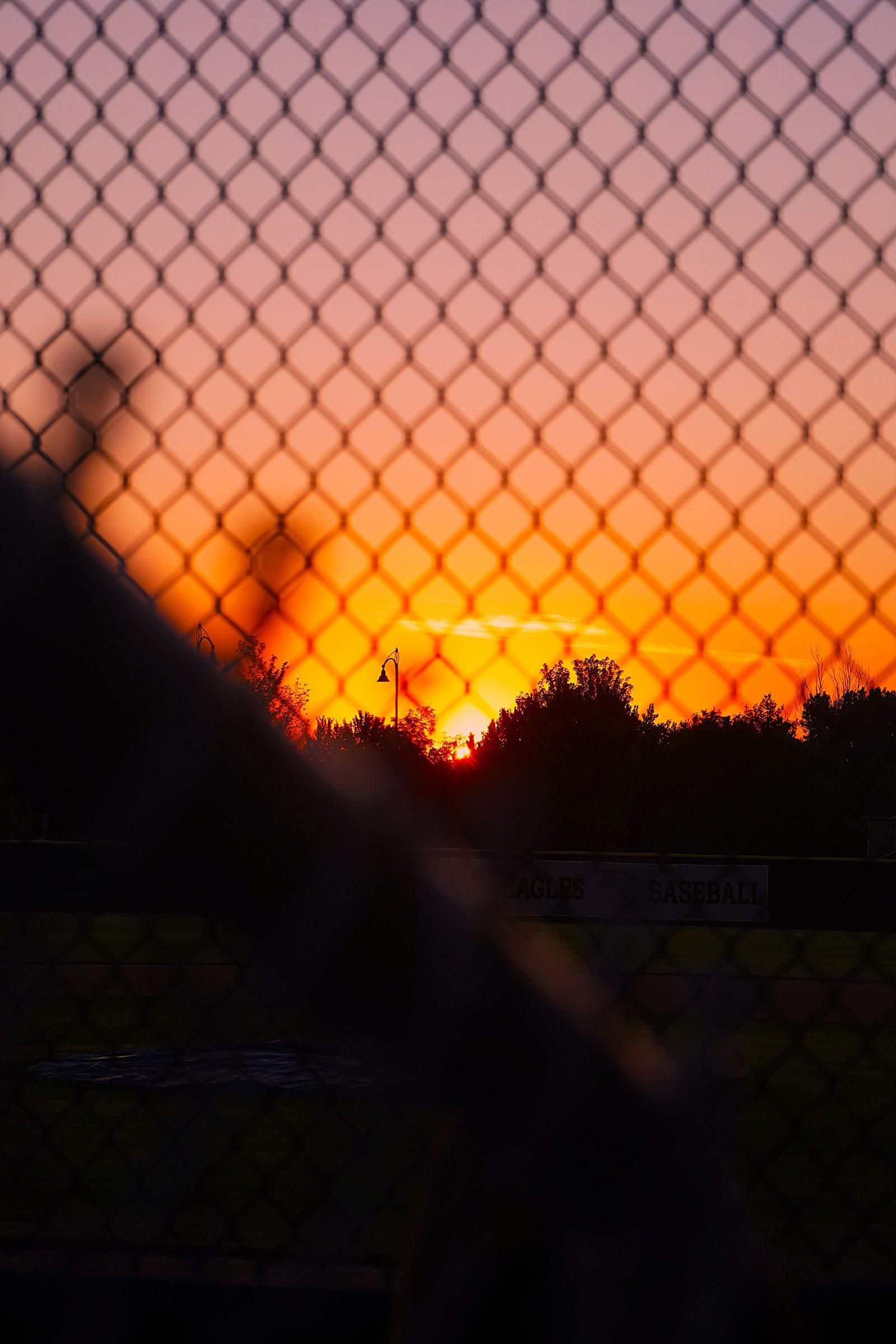 Sunset through a chain-link fence at a baseball field