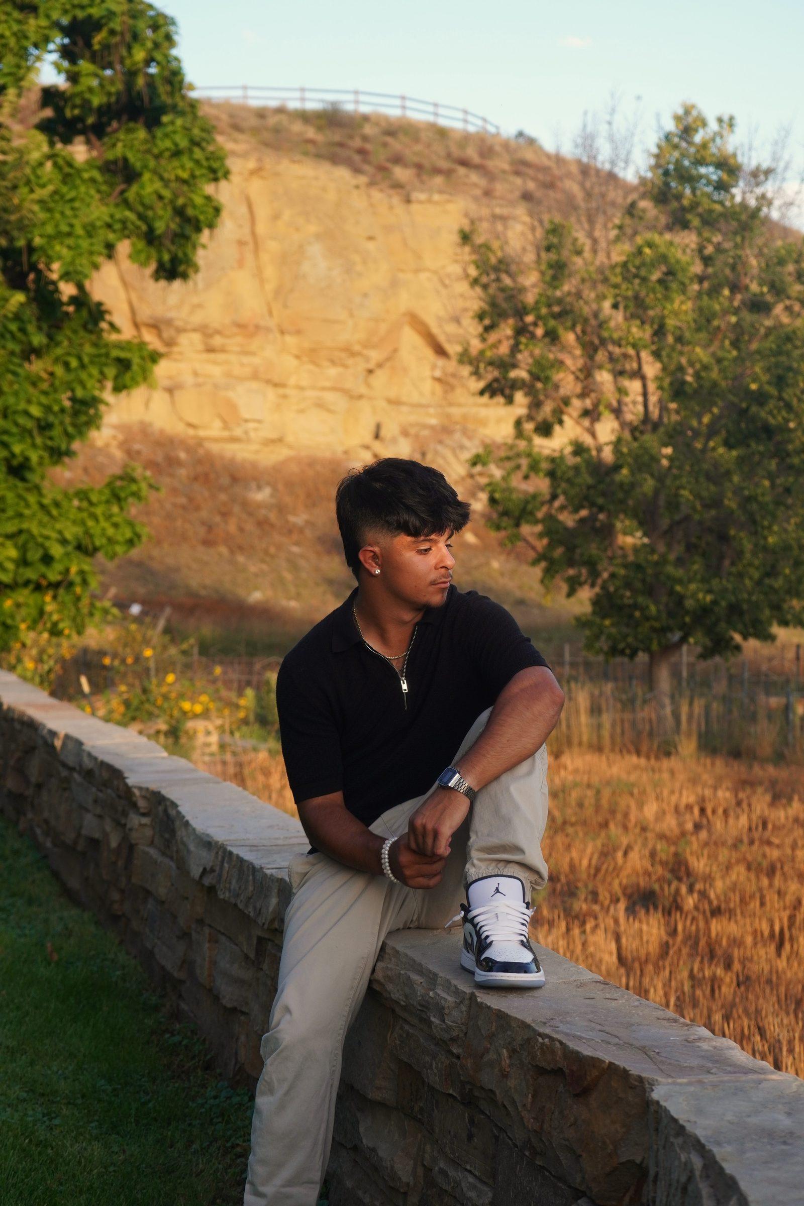 Senior portrait sitting on a stone wall at golden hour